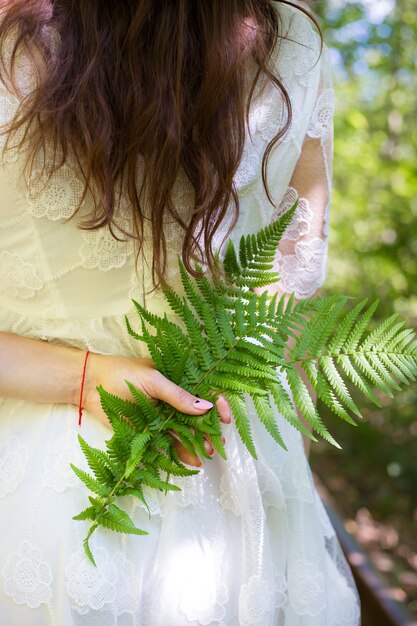 Fille en robe blanche, tenant des feuilles de fougère verte dans la forêt