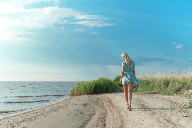 Une fille en robe bleue se promène le long du bord de mer