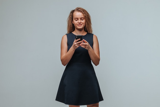 Une fille en robe bleue tape un message dans le téléphone sur un fond gris