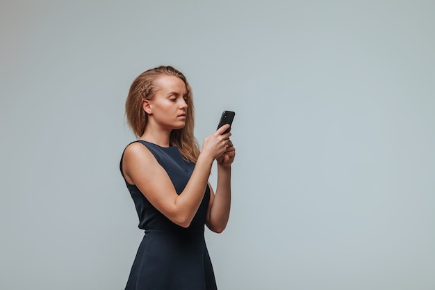 Une fille en robe bleue tape un message dans le téléphone sur un fond gris