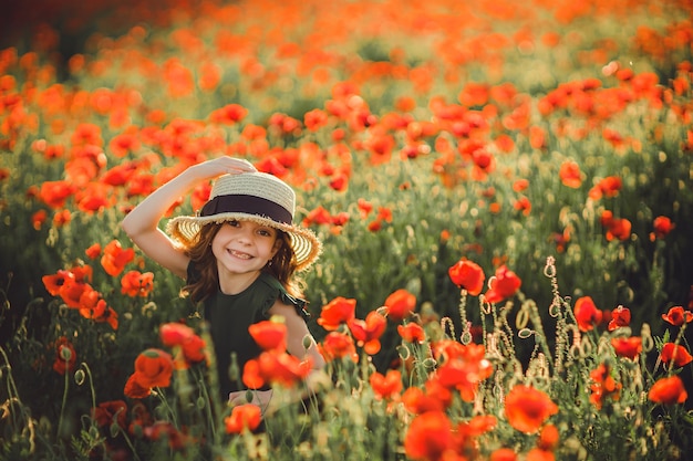 Fille en robe et chapeau de paille en plein air au champ de coquelicots au coucher du soleil