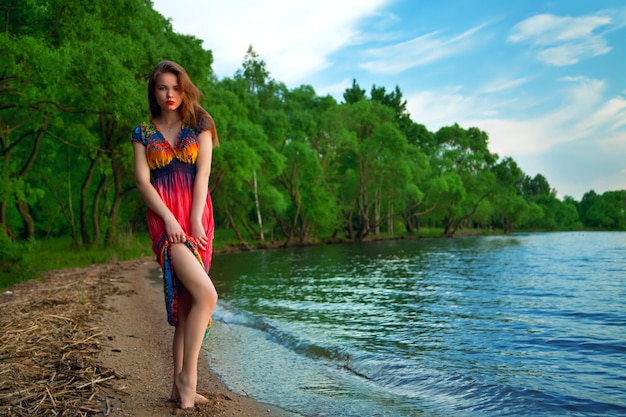 Fille en robe colorée à la mer hippies au coucher du soleil profitant d'une soirée d'été