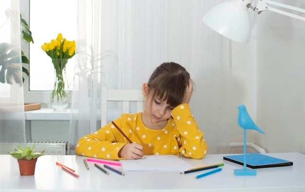 Une fille en robe jaune dessine dans sa chambre à son bureau avec des crayons de couleur Le concept de créativité et de développement des enfants Mise au point sélective