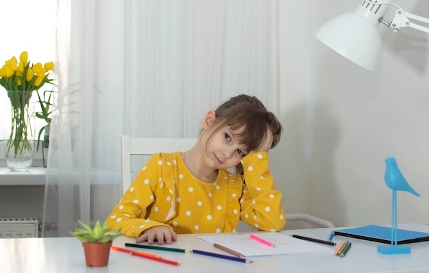 Une fille en robe jaune dessine dans sa chambre à son bureau avec des crayons de couleur Le concept de créativité et de développement des enfants Mise au point sélective