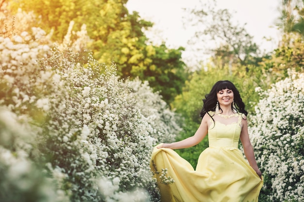 Une fille en robe jaune se tient entre la spirée en fleurs et le rayon de soleil brille sur elle.