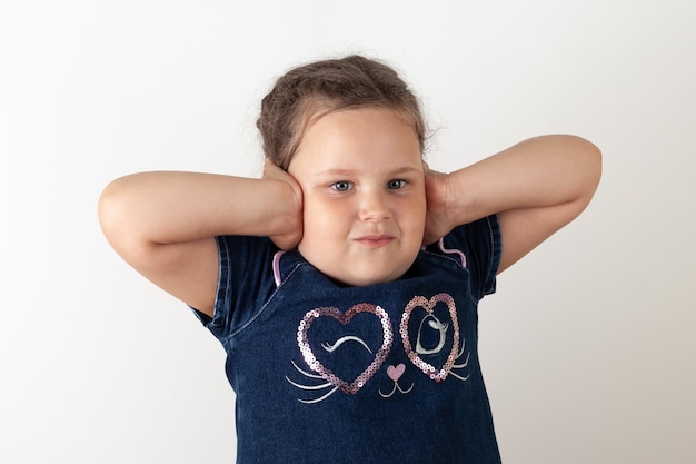 La fille à la robe en jean bleue s'est couverte les oreilles de ses mains, ne veut rien écouter