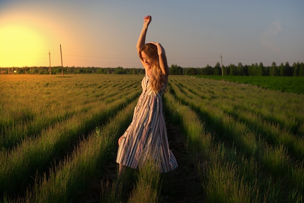 Une fille en robe légère dans un champ vert au coucher du soleil