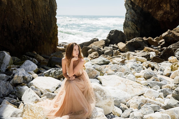 Fille en robe longue près des rochers et de l'océan