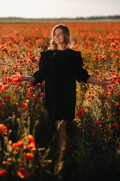 Une fille en robe noire sur un champ de pavot au coucher du soleil