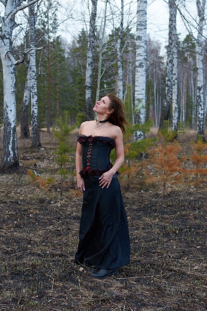 Une fille en robe noire dans la forêt.la fille est une sorcière dans un corset noir.