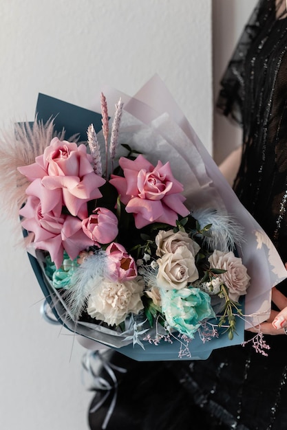 Une fille en robe noire tient un bouquet lumineux avec des fleurs bleues et roses Rose pivoine tulipe dianth