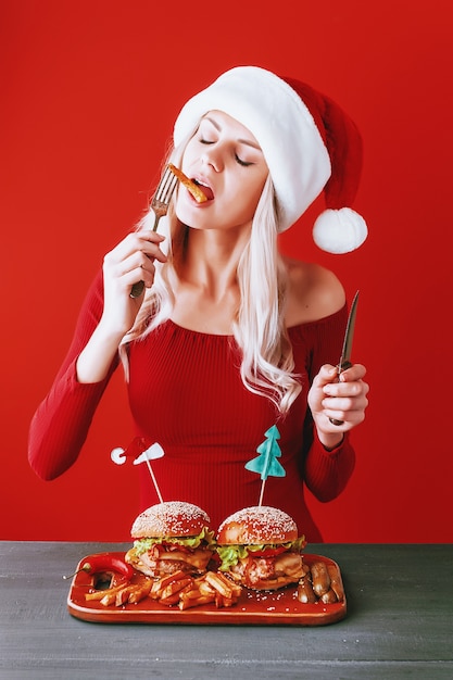 Fille en robe rouge et bonnet de noel avec burger à la main