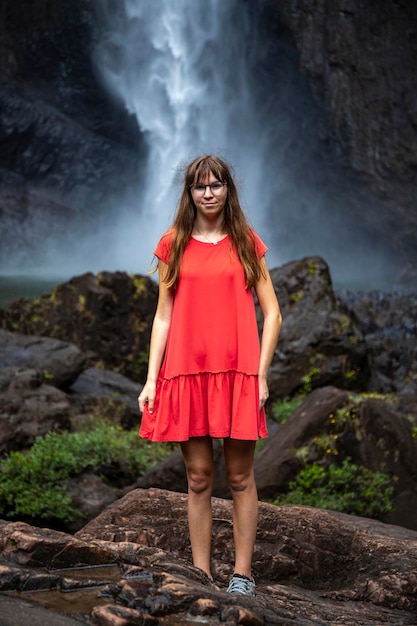 fille en robe rouge se tient sous une énorme cascade, vue spectaculaire sur les chutes de wallaman, queensland, aus