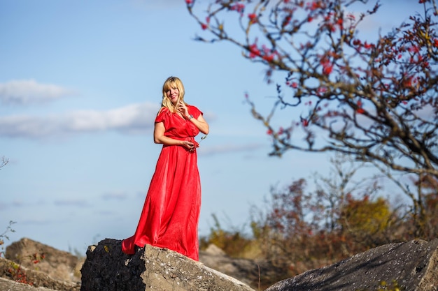 Fille en robe rouge sur la structure en ruine de roche ou de béton avec rowan sur fond d'automne