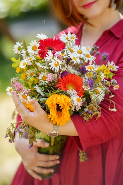 Une fille en robe rouge tient un magnifique bouquet de fleurs dans ses mains