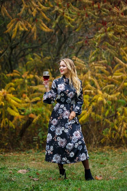 La fille en robe tient un verre de vin rouge dans la forêt d'automne