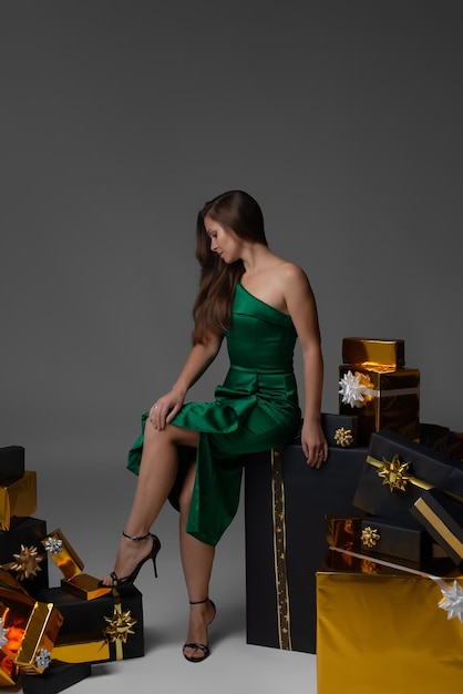 Photo une fille en robe verte sur un fond gris est assise sur une grande boîte à cadeaux