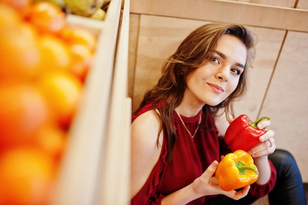 Fille en rouge tenant deux poivrons sur un magasin de fruits