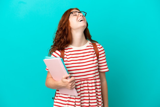 Fille rousse adolescente étudiante isolée sur fond bleu en riant