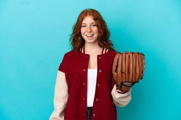 Fille rousse adolescente avec gant de baseball isolé sur fond bleu avec une expression faciale surprise