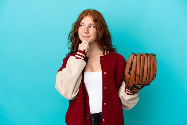 Fille rousse adolescente avec gant de baseball isolé sur fond bleu et levant