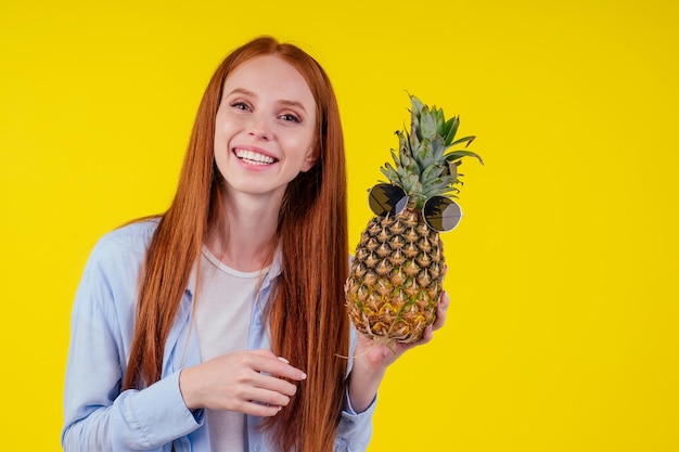 Fille rousse au gingembre s'amusant avec l'ananas sur fond de murs de couleur jaune studio.