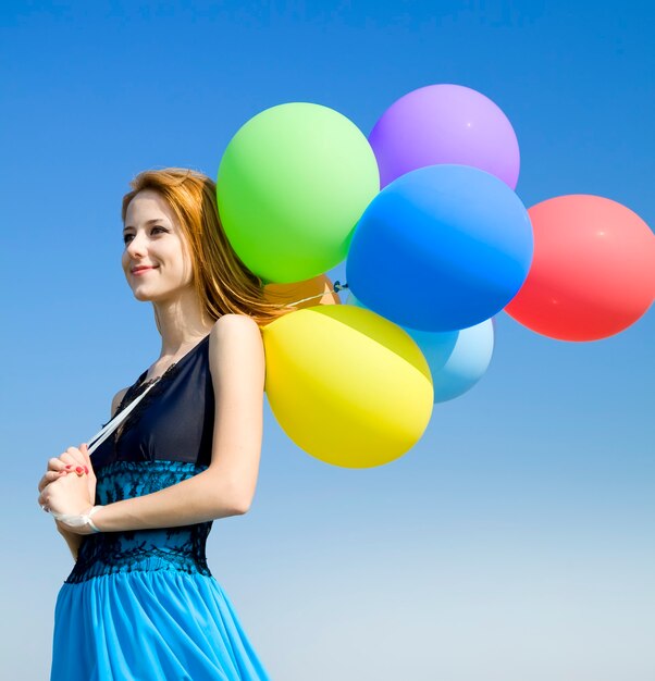 Photo fille rousse avec des ballons de couleur sur le ciel bleu.