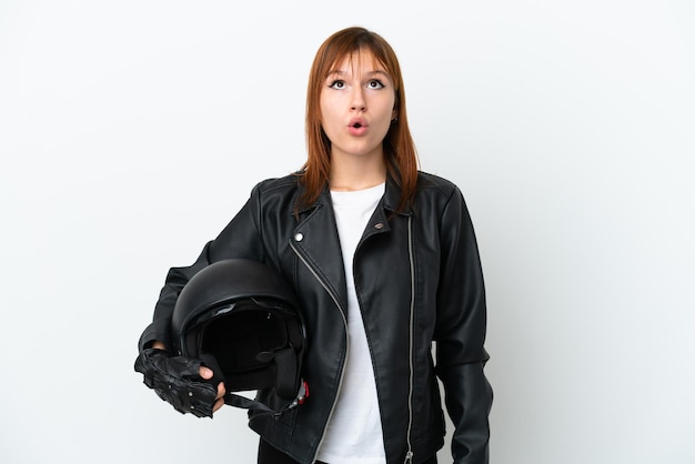 Fille rousse avec un casque de moto isolé sur fond blanc en levant et avec une expression surprise