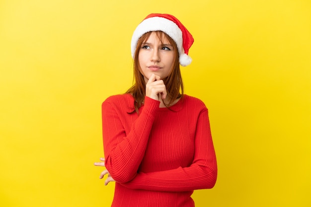 Fille rousse avec chapeau de Noël isolé sur fond jaune et levant