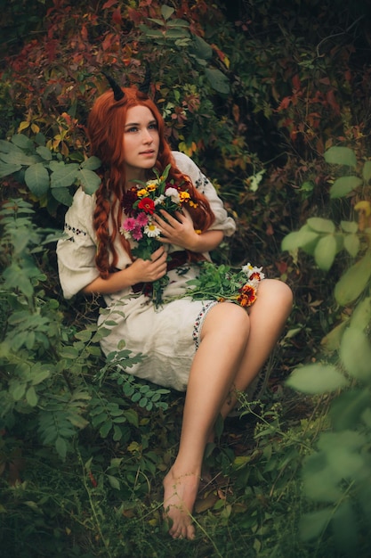 Fille rousse avec des cornes dans un vyshyvanka blanc dans le parc