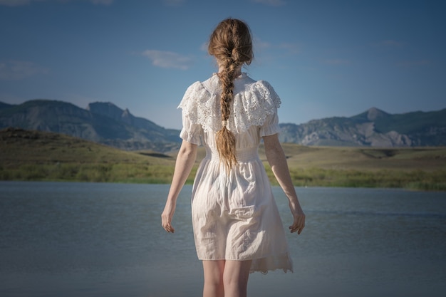 Fille rousse dans un champ de blé dans une robe blanche sourit un beau sourire