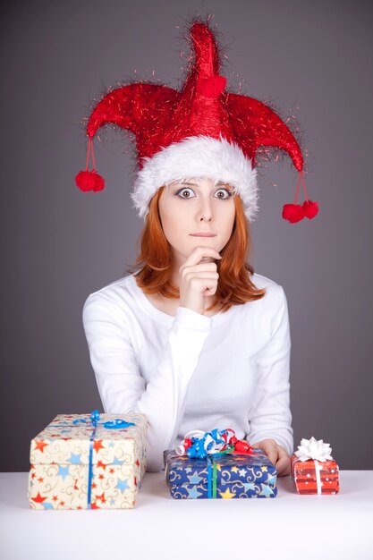 Fille rousse drôle au chapeau de Noël avec des coffrets cadeaux.