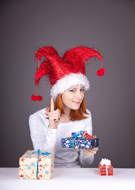 Fille rousse drôle au chapeau de Noël avec des coffrets cadeaux.