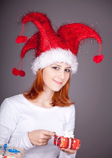 Fille rousse drôle au chapeau de Noël avec des coffrets cadeaux.