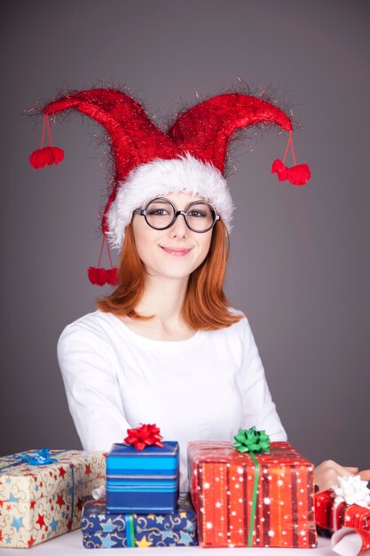 Fille rousse drôle en chapeau de Noël et lunettes avec coffrets cadeaux.