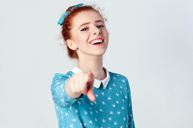 Fille rousse drôle en robe bleu clair ayant un doigt pointé vers la caméra et un sourire à pleines dents