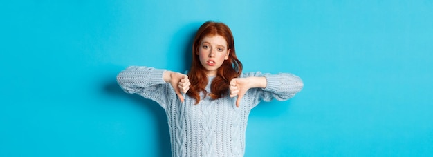 Fille Rousse Ennuyée Et Sceptique Montrant Les Pouces Vers Le Bas à L'air Indifférent Et Indifférent Debout Sur