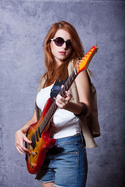 Fille rousse avec guitare près du mur