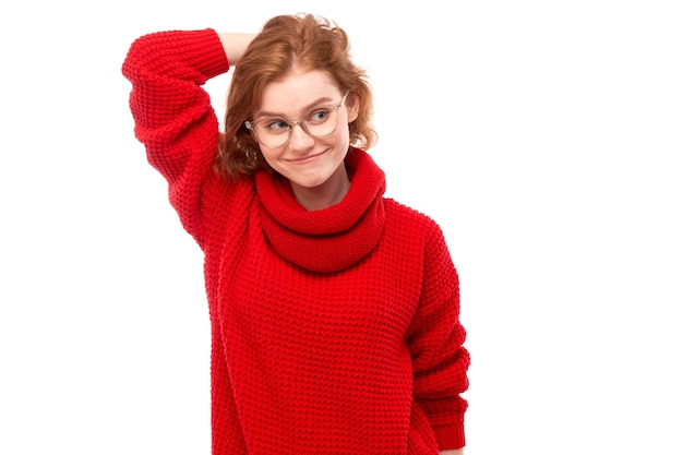 Une fille rousse intelligente en rouge et des lunettes touchant sa tête pense que les doutes prennent une décision isolée sur fond de studio blanc