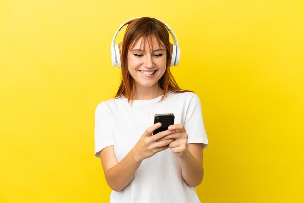 Fille rousse isolée sur fond jaune écoutant de la musique avec un mobile et regardant devant