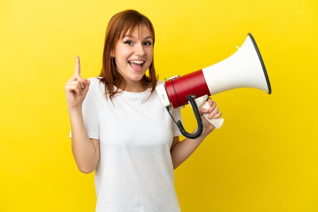 Fille rousse isolée sur fond jaune tenant un mégaphone et ayant l'intention de réaliser la solution