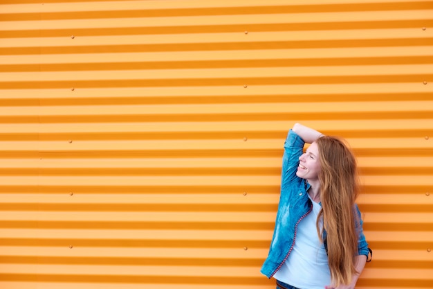 Fille rousse en jeans chemise près du mur orange