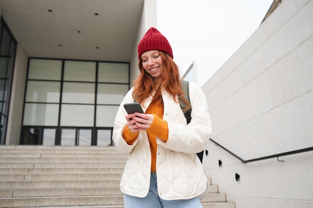 Photo fille rousse jeune femme touriste avec sac à dos tient le smartphone cherche l'itinéraire sur l'application mobile