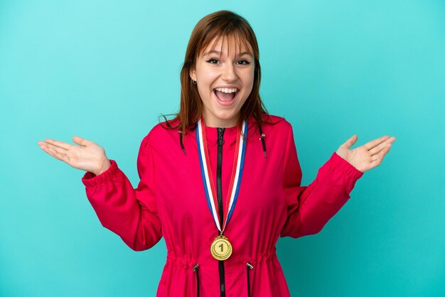 Photo fille rousse avec des médailles isolées sur fond bleu avec une expression faciale choquée