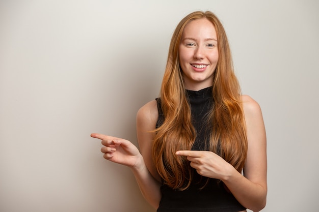 Une fille rousse sur un mur blanc offre des possibilités de pointer du côté du doigt à l'espace libre de copie pour l'annonce de contenu promotionnel.