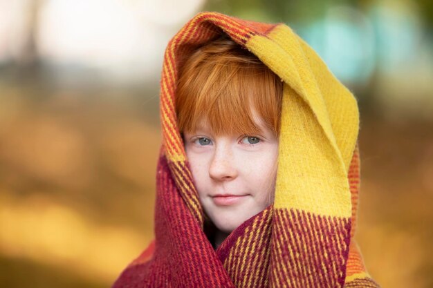 Une fille rousse s'est enveloppée dans une couverture de laine dans un parc d'automne Enfant en automne