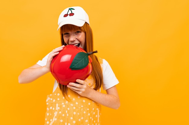 Fille rousse avec un sac à main rouge en forme de pomme grimace