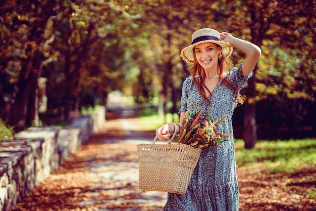 Une fille rousse souriante marche seule dans un parc d'automne par une chaude journée ensoleillée tout en tenant un sac à main l'été indien