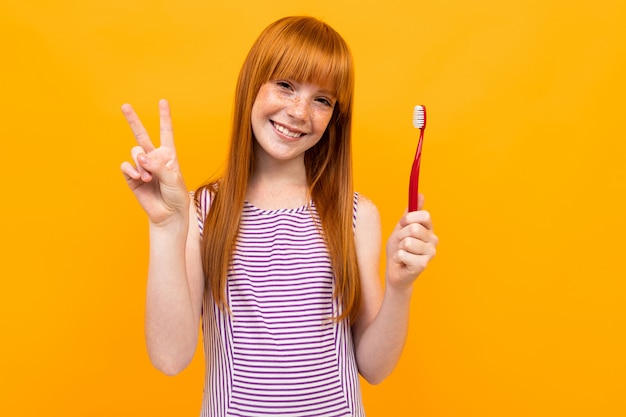 Fille Rousse Sourit Et Tient Une Brosse à Dents Dans Les Mains Sur Un Fond Jaune