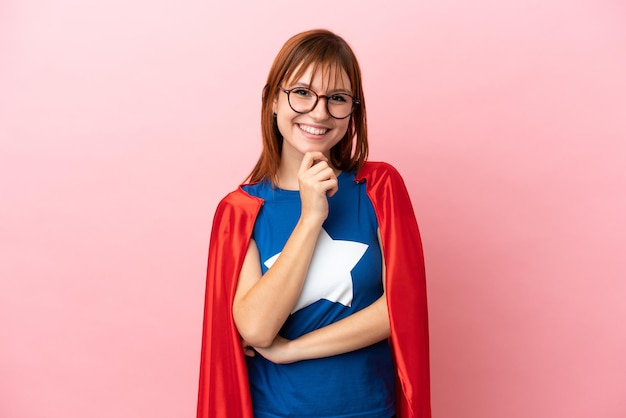 Fille rousse de super héros isolée sur fond rose avec des lunettes et souriant